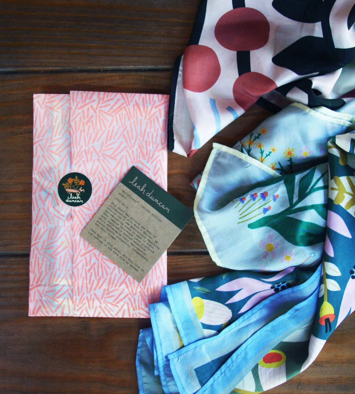 Colorful folded silk scarves with floral Wildflower design and Leah Duncan label on wooden surface