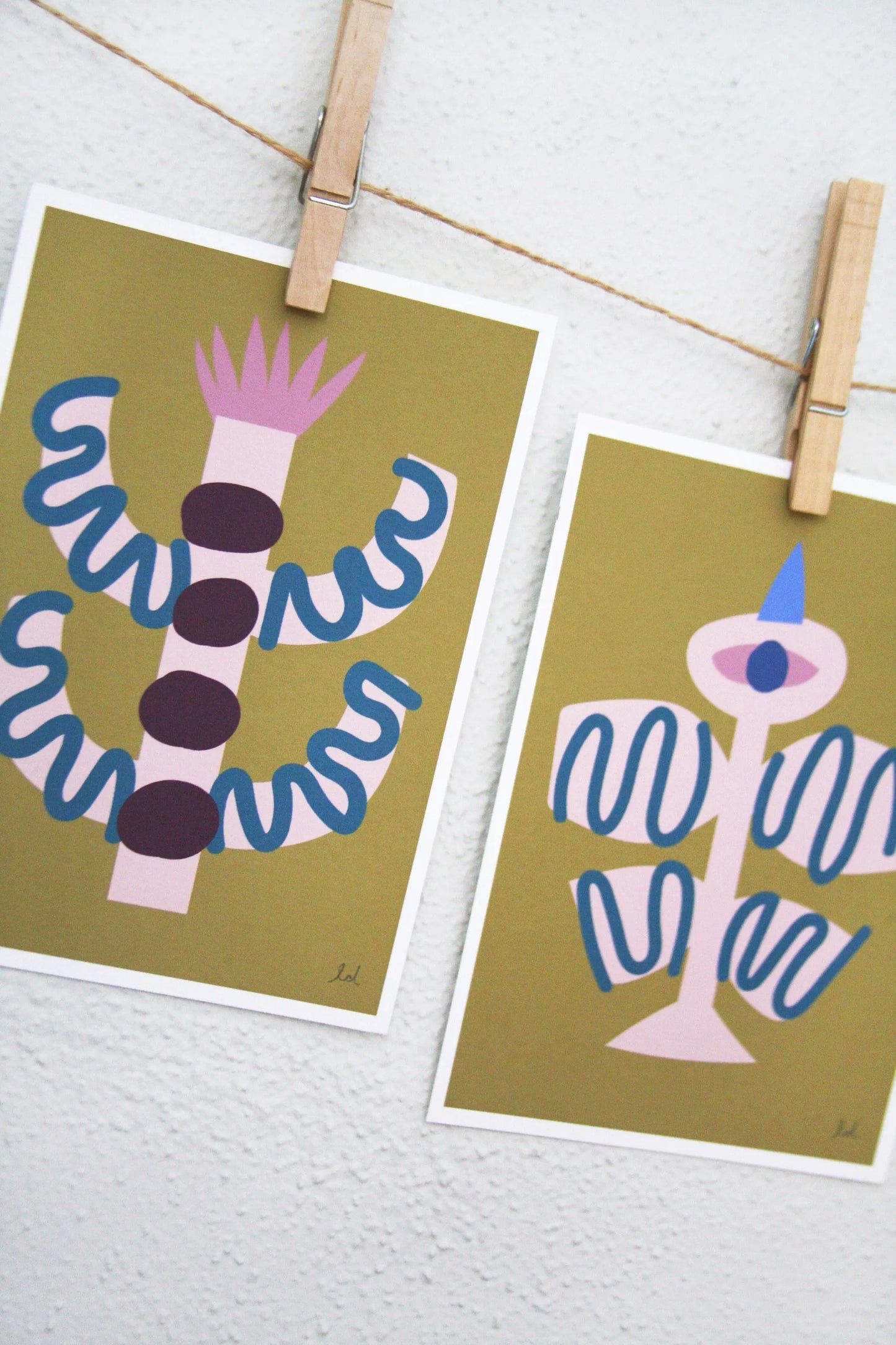 Two bird and flower abstract prints in ochre tones clipped on a string against a white wall