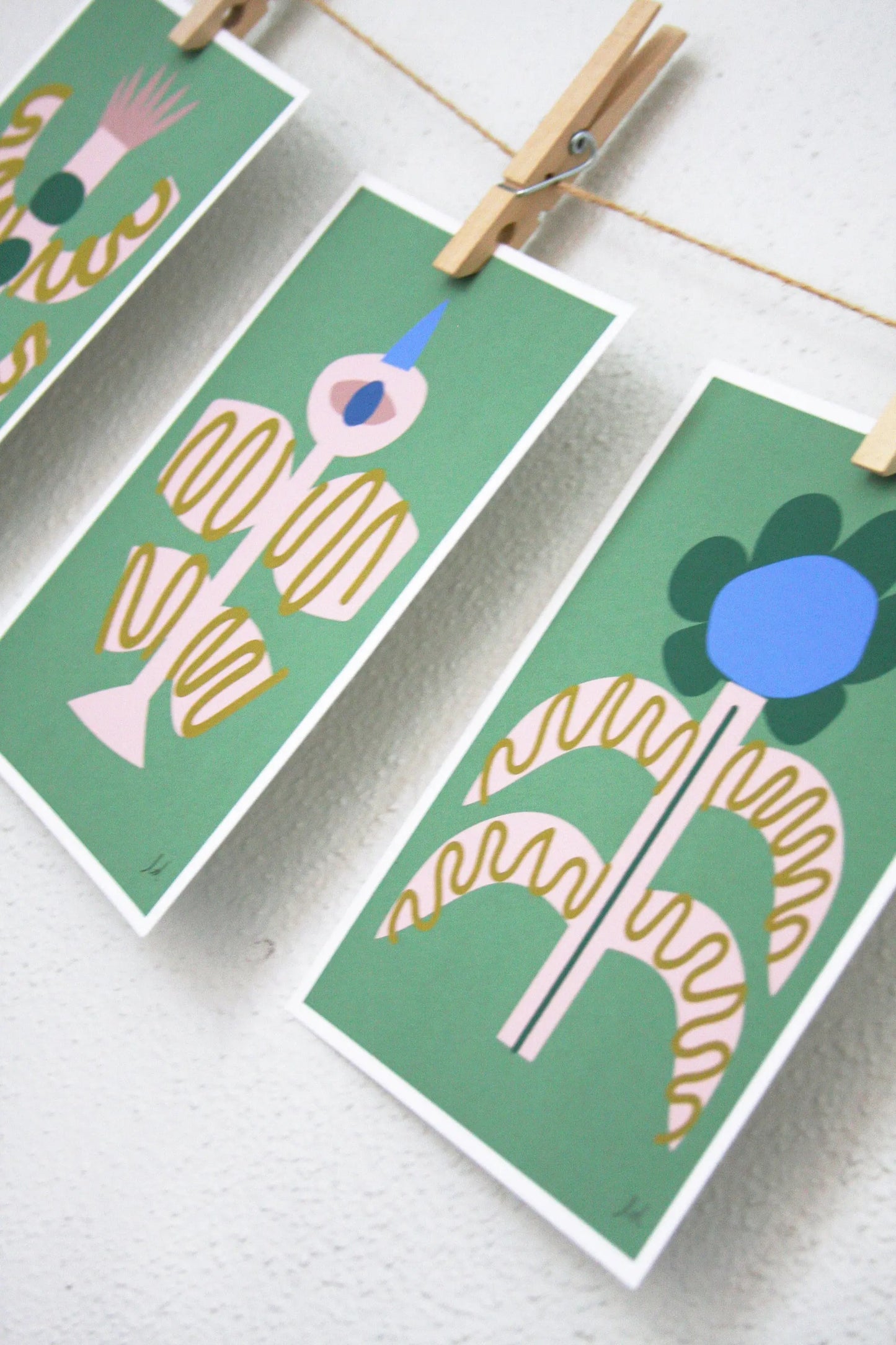 Three green modern folk art prints of abstract birds and flowers hanging with clothespins on a string