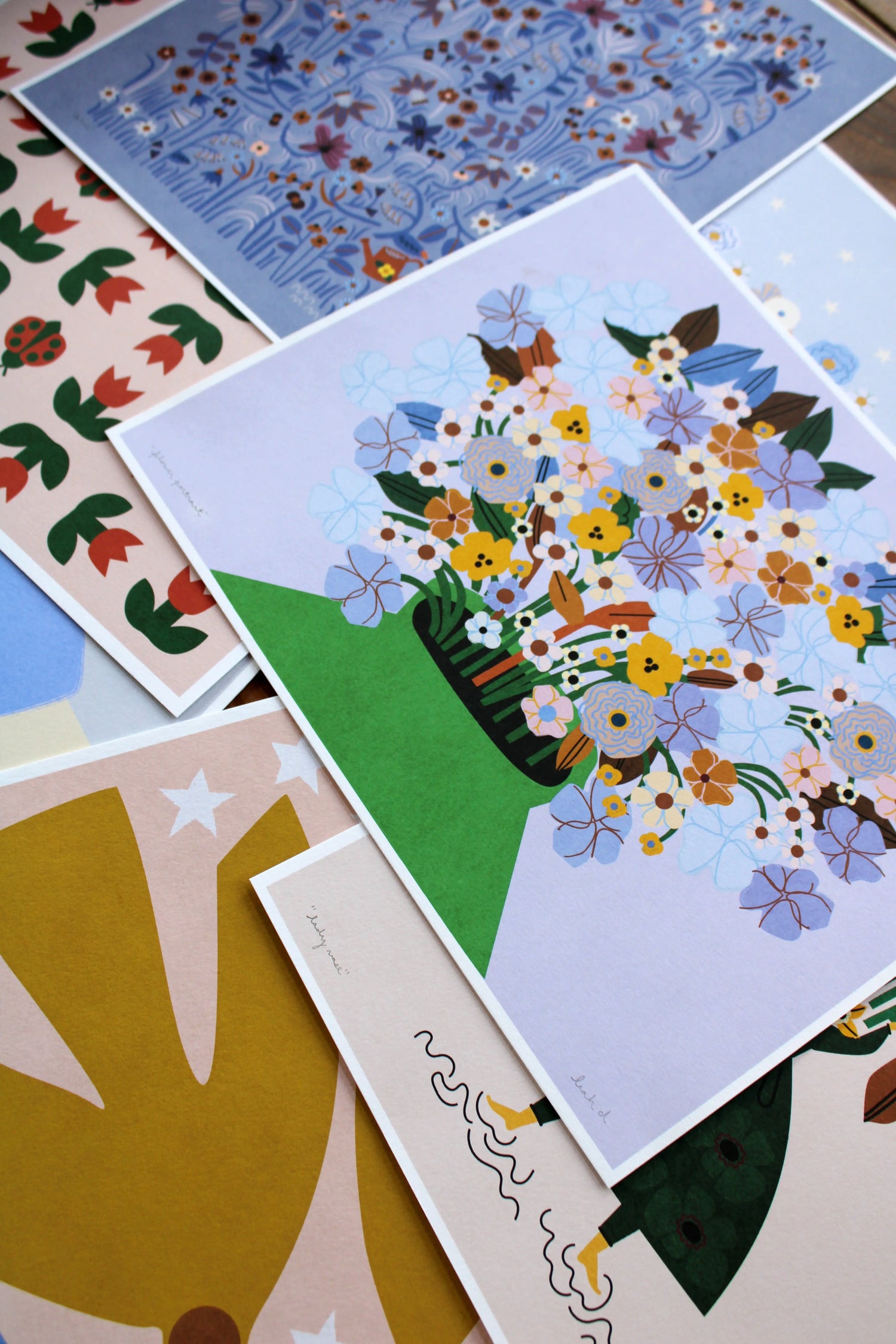stack of signed art prints featuring florals, girls, and birds