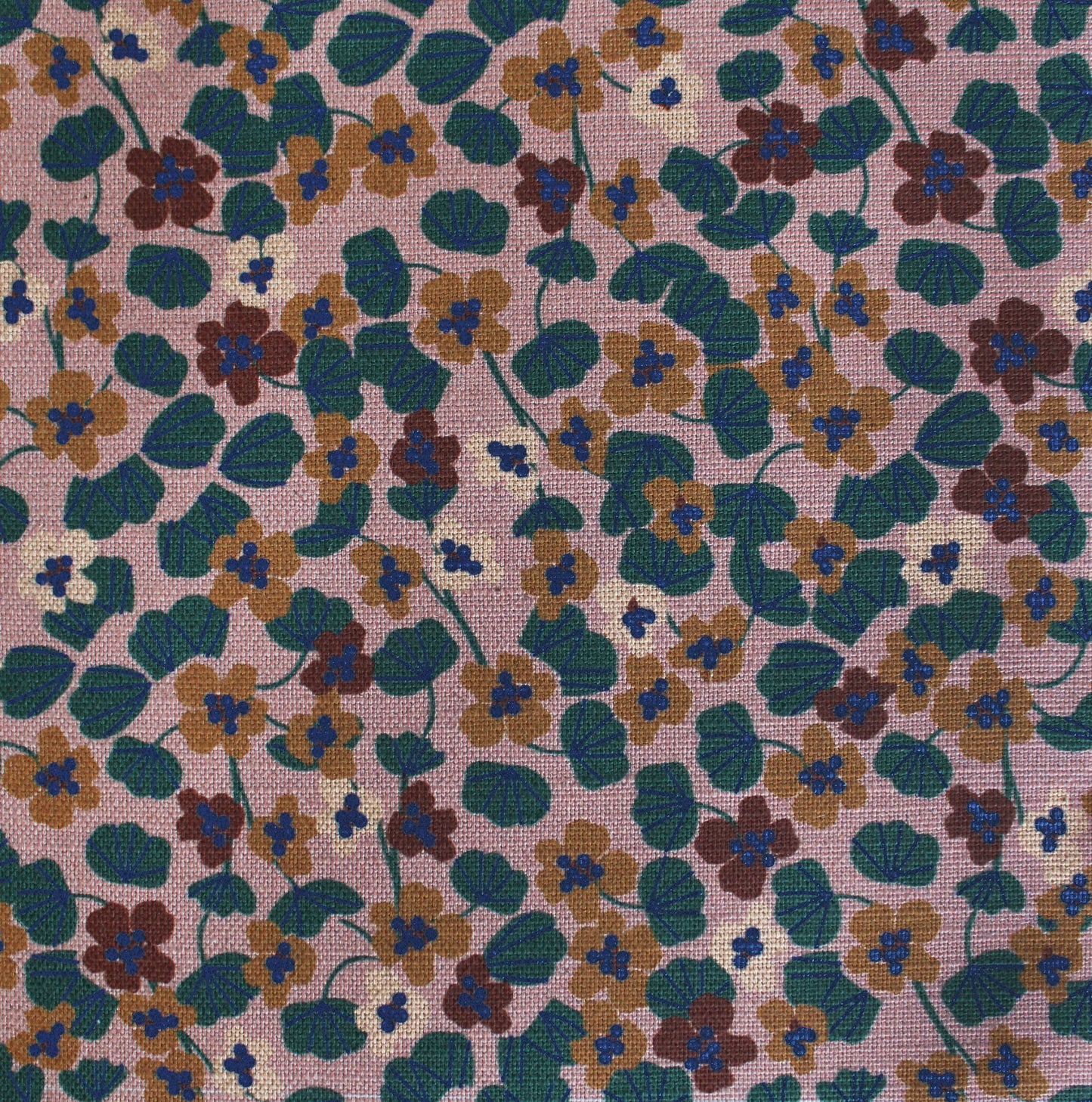 Floral patterned fabric with small flowers in green, brown, and blue on a pink background