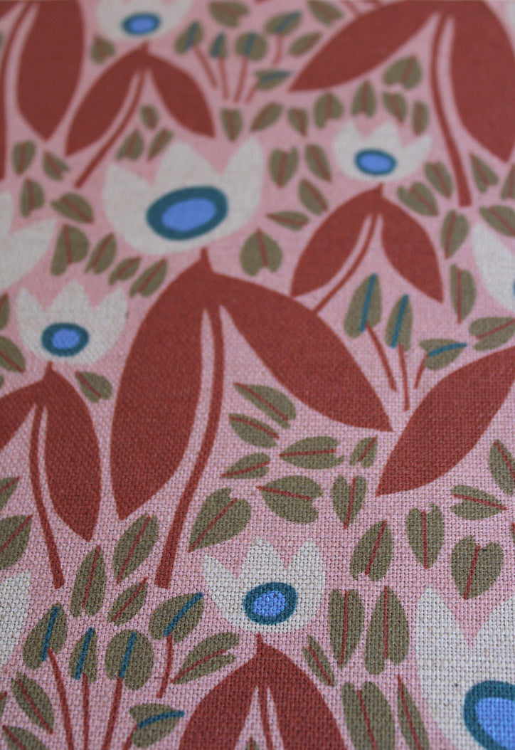 Close-up of fabric with floral pattern featuring red, green, and blue colors on a pink background.