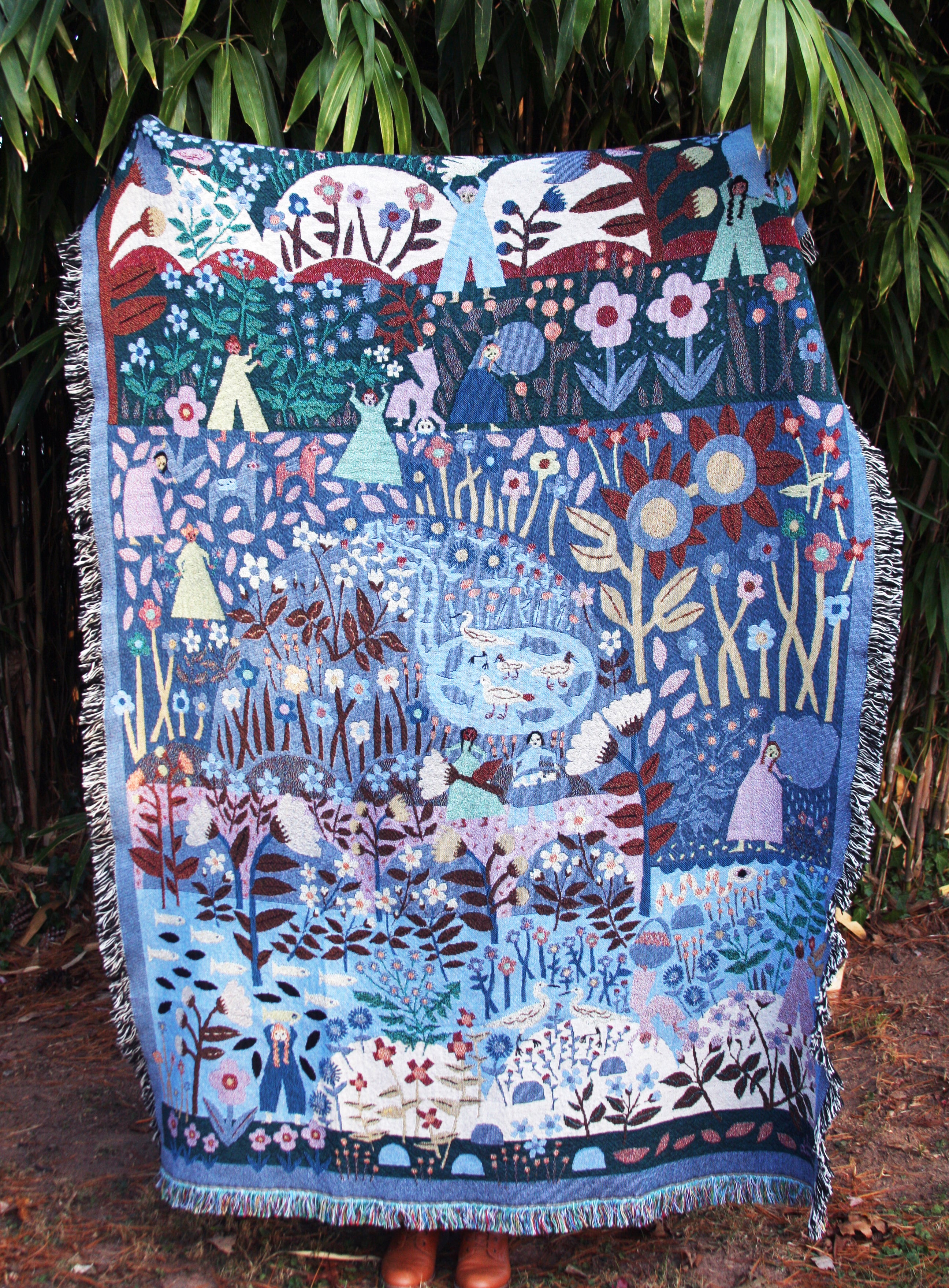 A woven blanket with a floral and nature-themed design, featuring various colors such as blue, white, and brown, displayed as a tapestry.