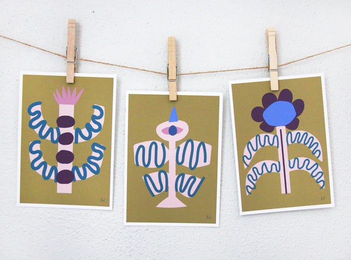 Three mid-century modern bird and flower prints with abstract shapes in ochre, blue, and purple tones hanging on a string